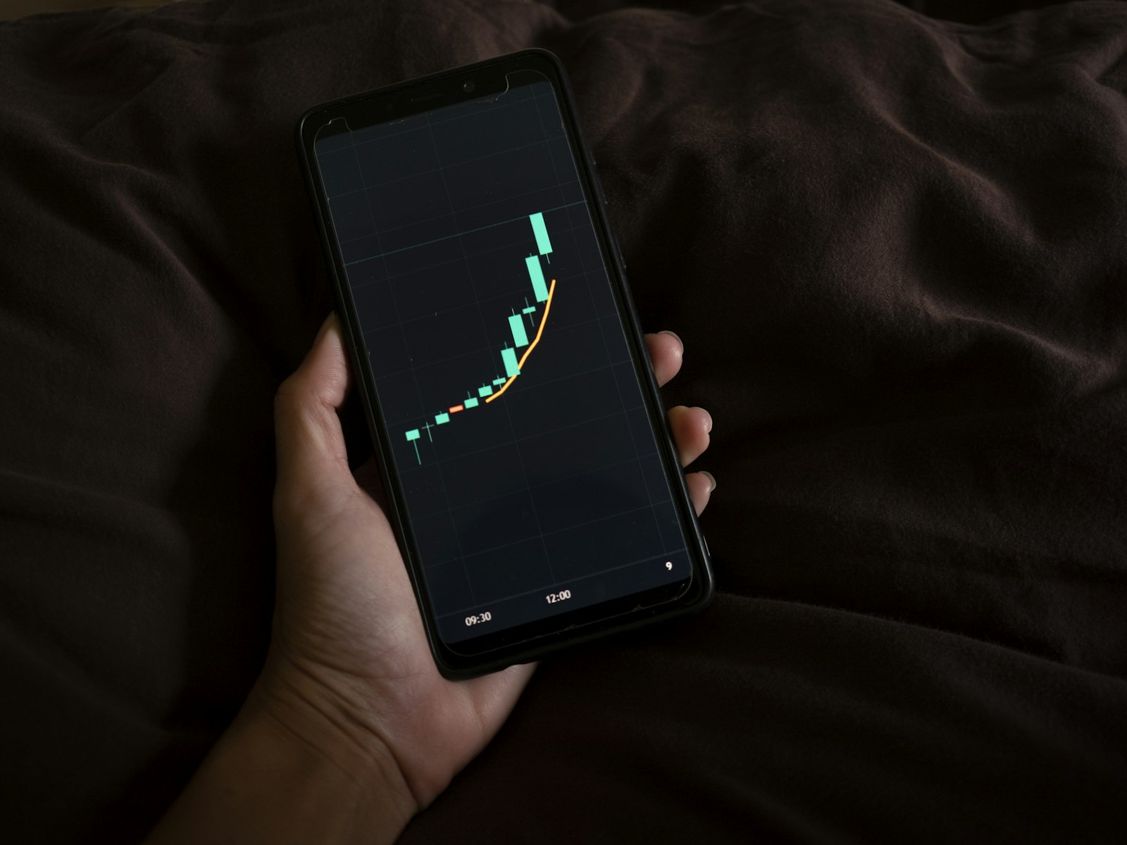 A person checking a rising stock chart on their phone in low light