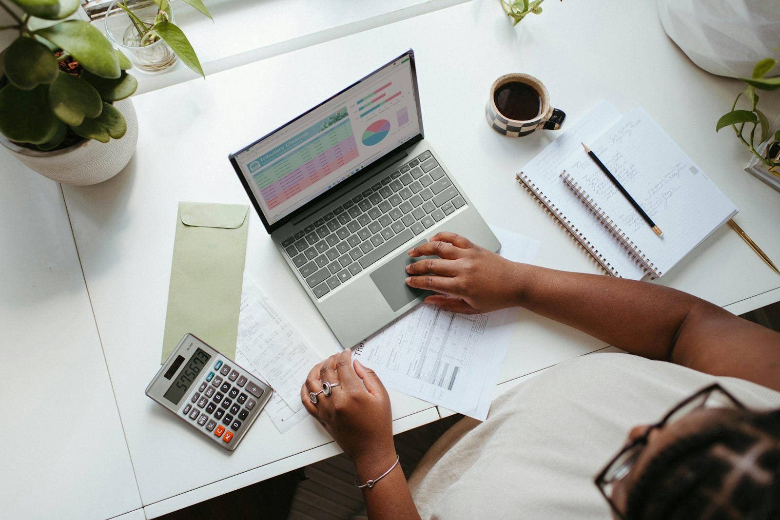 A desk with a laptop showing charts, a calculator, notebook and coffee, representing comparing ISA fees between Lightyear and InvestEngine