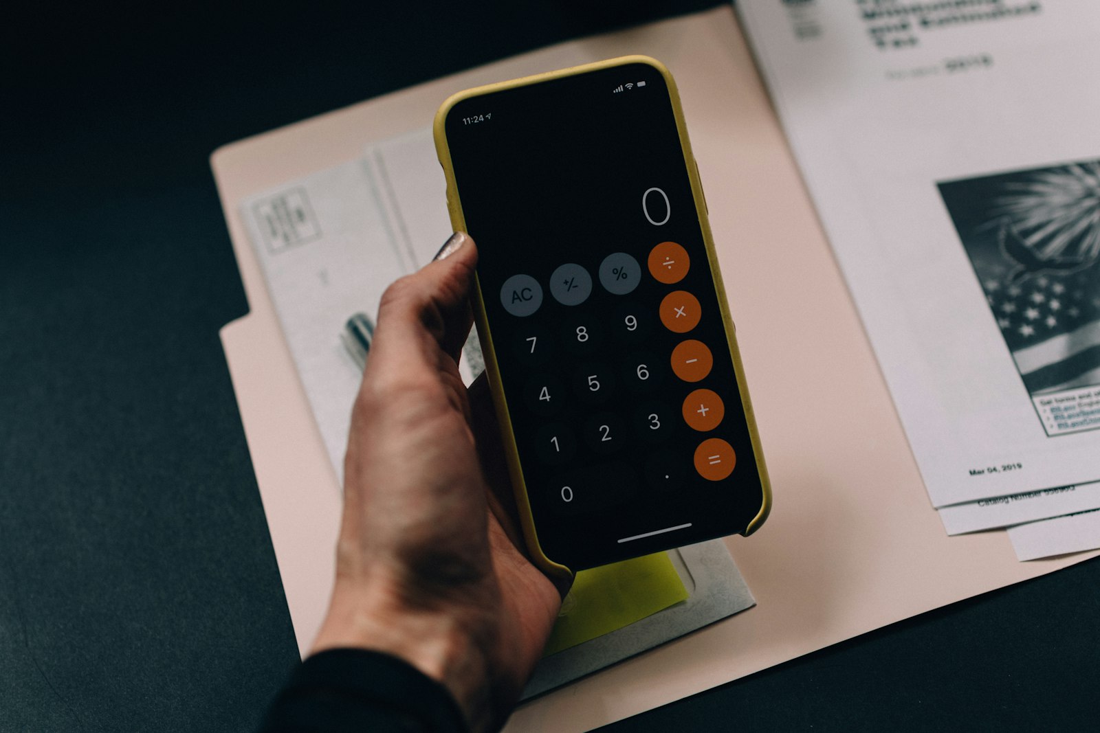 A hand holding a smartphone showing a finance calculator app over paperwork on a desk